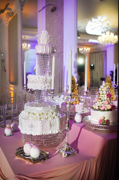 Bolo de casamento branco de três camadas decorado com flores creme em um carrinho.