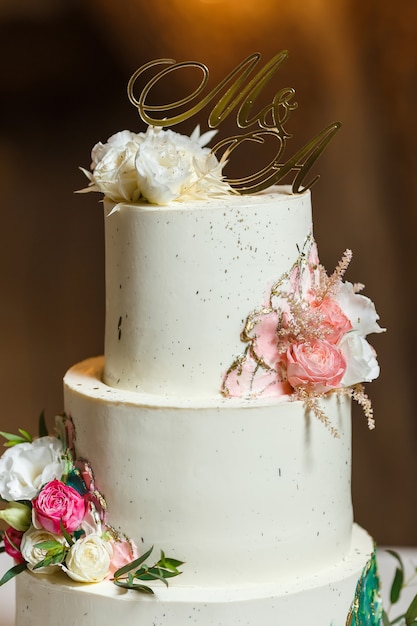 Bolo de casamento branco elegante decorado com flores frescas e cartola de ouro.