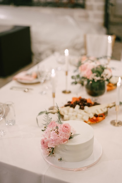 Bolo de casamento branco fica em um prato na mesa ao lado de velas acesas