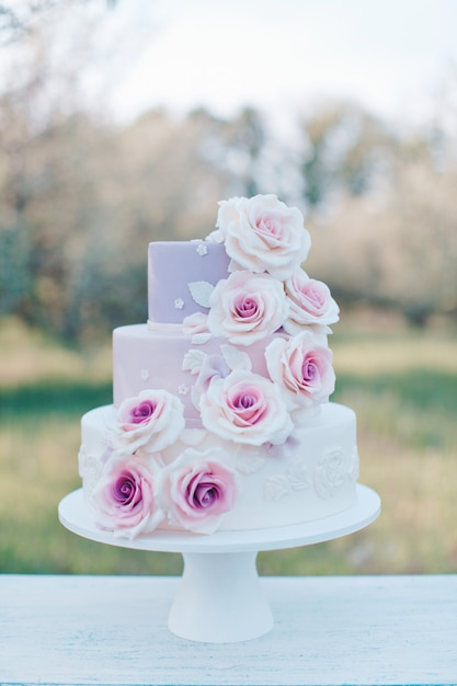 Bolo de casamento em tons pastel decorado com rosas cor de rosa realistas sobre um fundo desfocado do jardim, foco seletivo