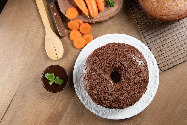 Bolo de cenoura brasileiro com cobertura de chocolate na mesa de madeira com cenoura ao fundo vista superior