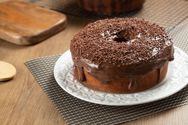 Foto bolo de cenoura brasileiro com cobertura de chocolate na mesa de madeira com cenoura ao fundo