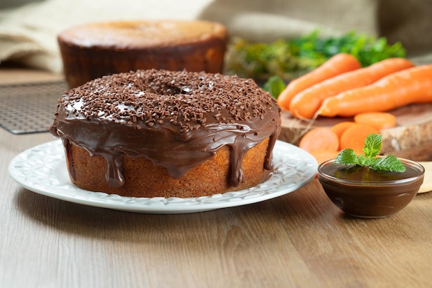 Bolo de cenoura brasileiro com cobertura de chocolate na mesa de madeira com cenoura ao fundo