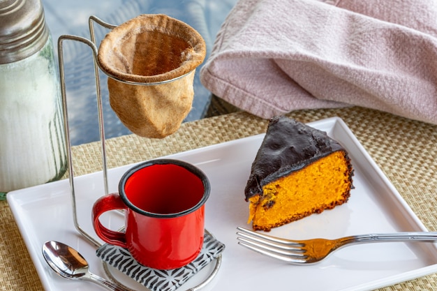 Bolo de cenoura com cobertura de chocolate, acompanhado de uma xícara de café.