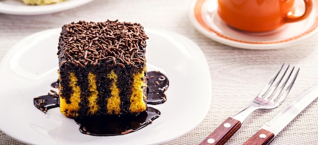 Bolo de cenoura com cobertura de chocolate pingando no prato servido com café com leite e outros doces padaria doce barco da tarde brasileira