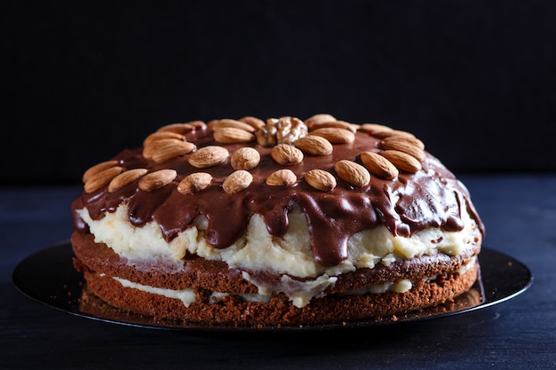 Bolo de chocolate caseiro com creme de leite e amêndoas em fundo preto de madeira.