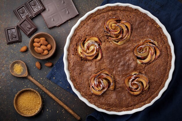 Bolo de chocolate caseiro com frangipane e flores de maçã em uma superfície de concreto escuro