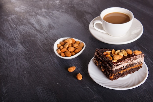 Bolo de chocolate com caramelo, amendoim e amêndoas em um fundo preto de madeira.