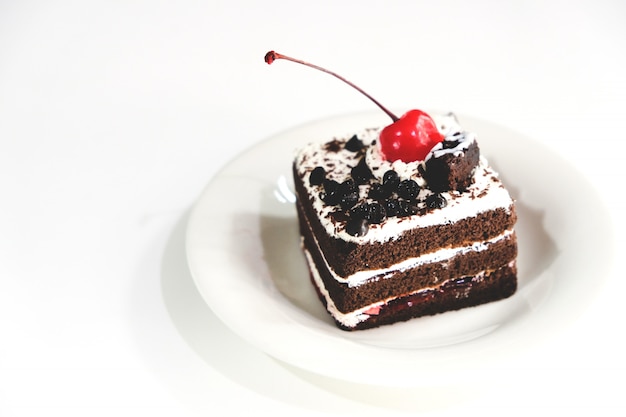 Bolo de chocolate com cerejas vermelhas sobre um fundo branco.