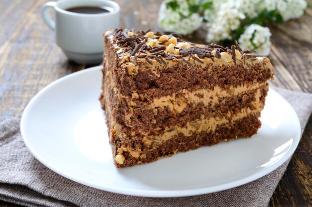 Bolo de chocolate com creme de nozes em uma mesa de madeira. Um pedaço de bolo em um prato e uma xícara de café.