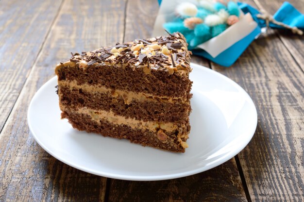 Bolo de chocolate com creme de nozes em uma mesa de madeira. Um pedaço de bolo em um prato