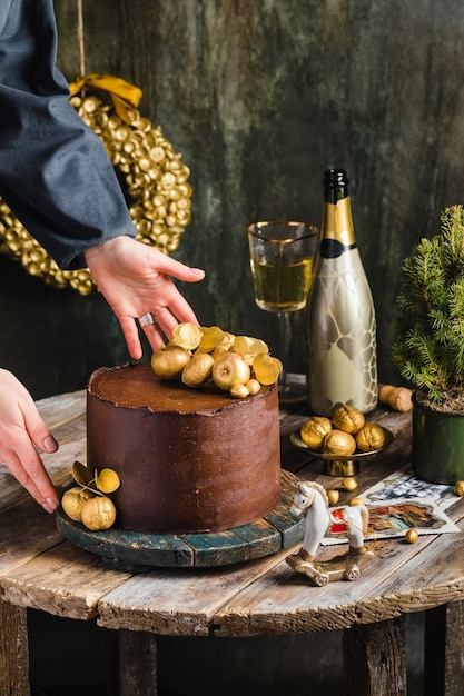 Bolo de chocolate com decoração dourada champanhe atrás de mulher em estilo rústico com foto de alta qualidade