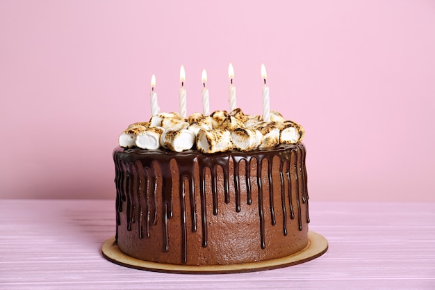 Bolo de chocolate com marshmallow e velas na superfície rosa