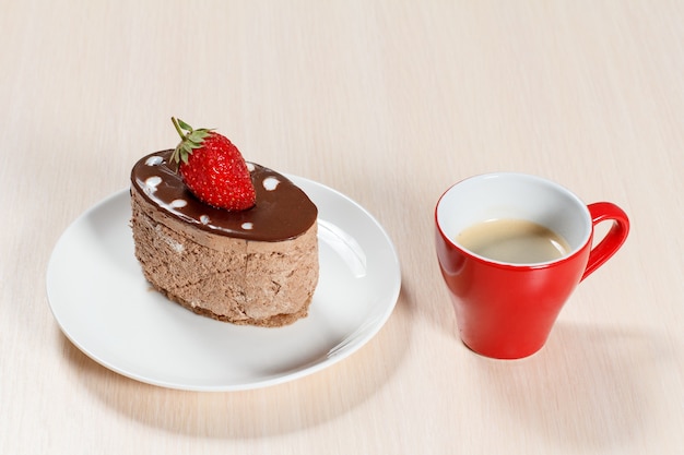 Bolo de chocolate com morango no prato branco e uma xícara de café em uma mesa de madeira