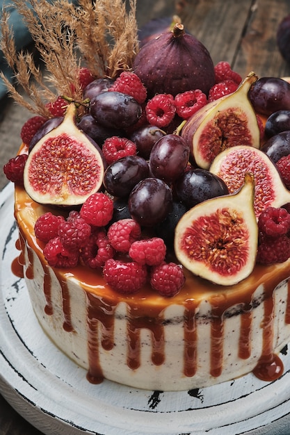 Bolo de chocolate com recheio de framboesa, decorado com figos frescos, uvas e framboesas. Bolo rústico em uma mesa de madeira.