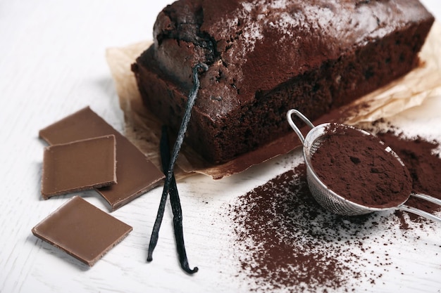 Bolo de chocolate com vagens de baunilha de cacau em pó na mesa branca