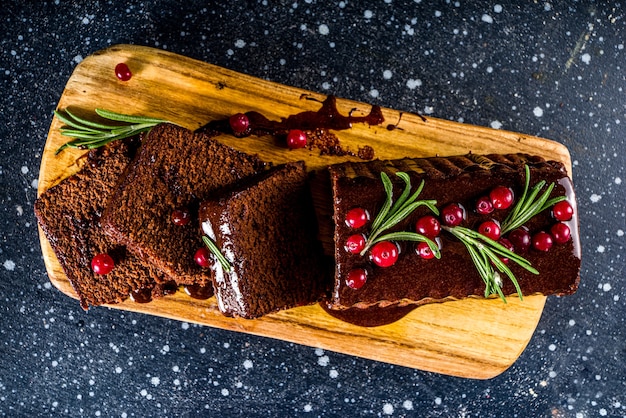 Bolo de chocolate de gengibre em fundo festivo. bolo de gengibre tradicional com cobertura de chocolate amargo, cranberry e alecrim, na mesa decorada de natal, copie o espaço