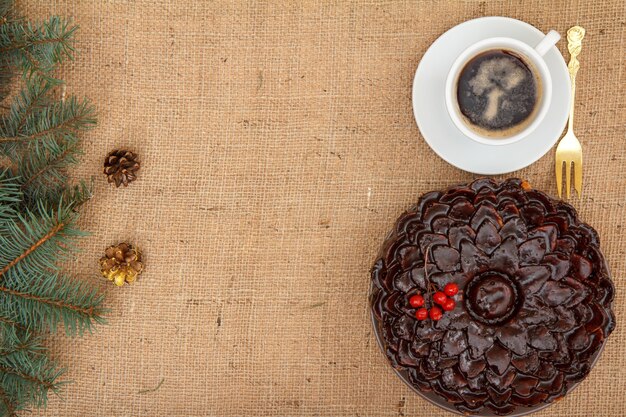 Bolo de chocolate decorado com ramo de viburno, xícara de café com ramo de abeto na mesa com ramo de abeto e serapilheira. Vista do topo. Conceito de feliz Natal.