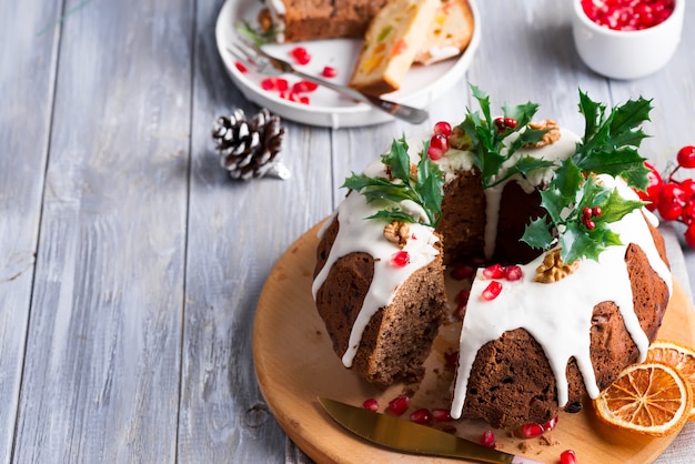 Bolo de chocolate em fatias de Natal com glacê branco, galhos de azevinho e miolo de romã, um cinza de madeira