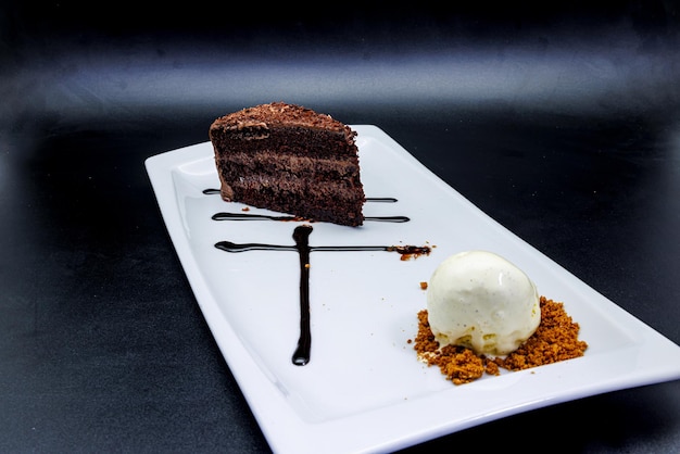 Foto bolo de chocolate em um prato branco com sorvete em fundo preto