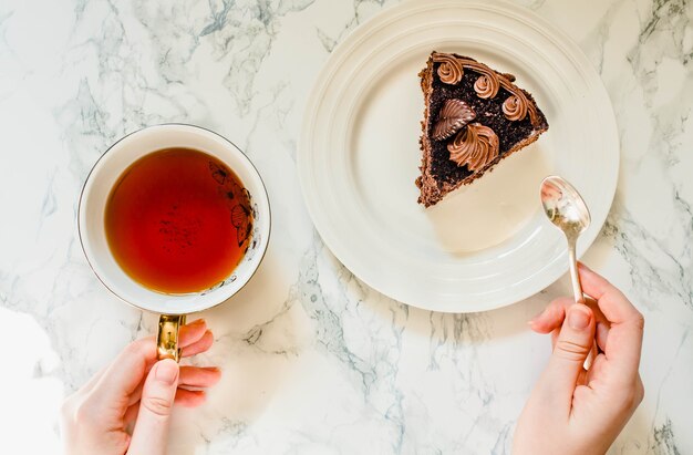 Bolo de chocolate escuro com cobertura de chocolate para férias e ouro xícara de chá. café da manhã doce. mãos de mulher jovem. processo de comer. vista do topo.