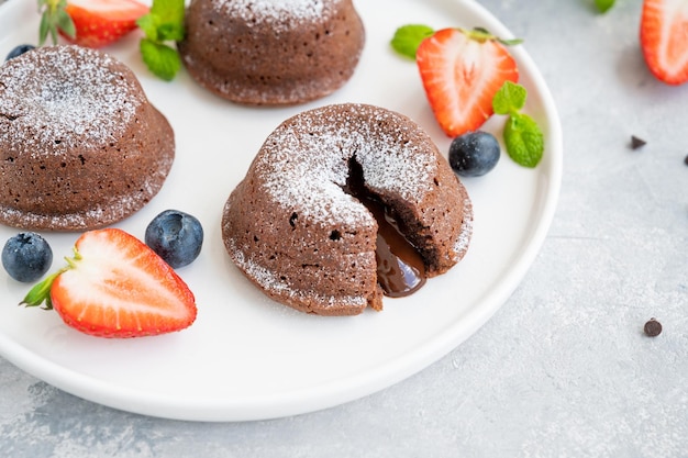 Bolo de chocolate fondant lava com frutas frescas em um prato sobre um fundo cinza.