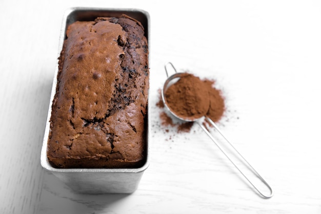 Bolo de chocolate na assadeira com cacau em pó na mesa branca