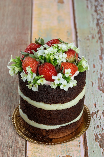 Bolo de chocolate nu, recheado com brigadeiro de coco. Decorado com morangos e flores brancas kalanchoe (foto vertical).