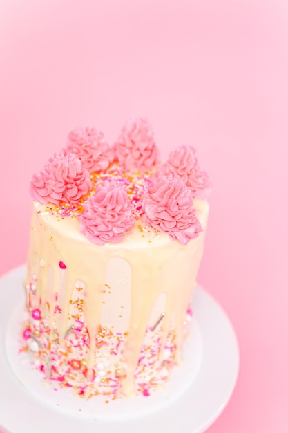 Foto bolo de creme de manteiga rosa e branco com granulado rosa e gotejamento de ganache de chocolate branco.