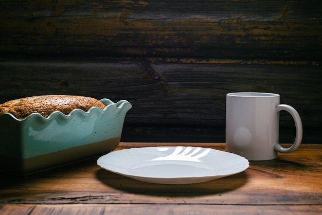Bolo de esponja caseiro em copo branco de molde de cerâmica azul e prato branco na mesa de madeira
