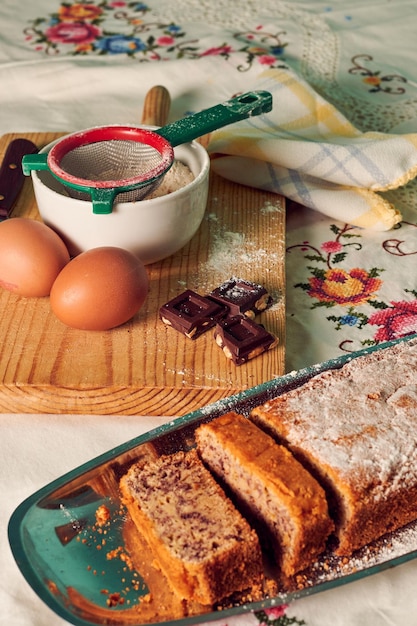 Bolo de esponja caseiro em uma toalha de mesa branca com alguns ingredientes ovos chocolate e farinha