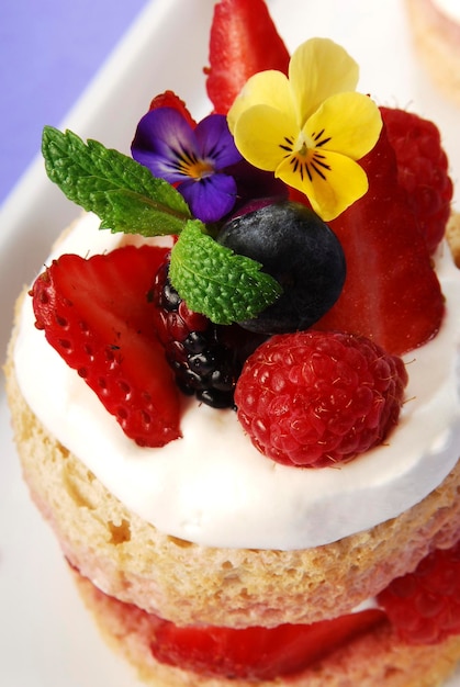 bolo de esponja em camadas com frutas vermelhas e flores comestíveis chantilly em fundo de verão lilás