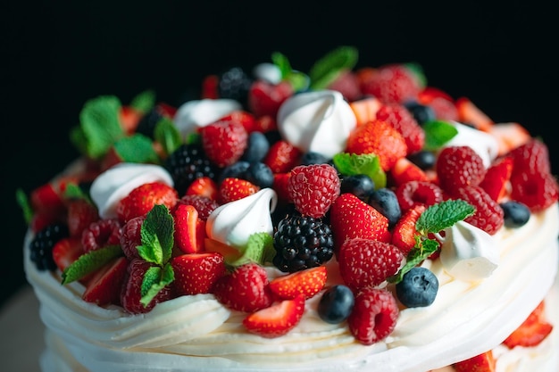 Foto bolo de frutas. bolo decorado com frutas em um carrinho de madeira em um fundo preto.