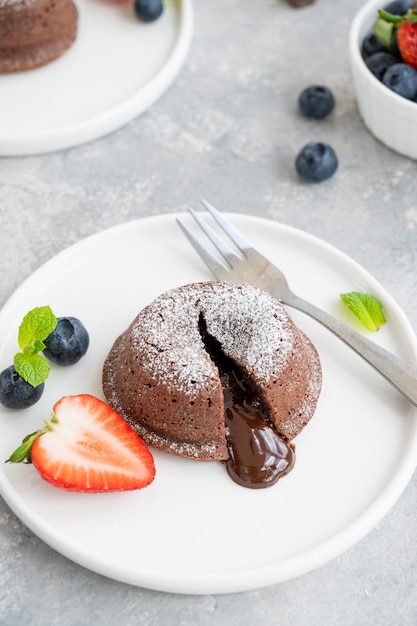 Bolo de lava fondant de chocolate com frutas frescas em um prato em um fundo cinza