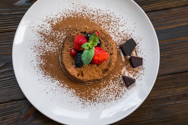 Bolo de lava fondant de chocolate decorado com morangos e cacau em pó em um fundo de madeira