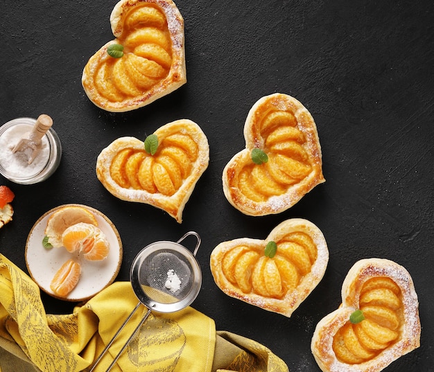 Bolo de massa folhada em forma de coração com fatias de tangerina sobre uma mesa escura com guardanapo amarelo para