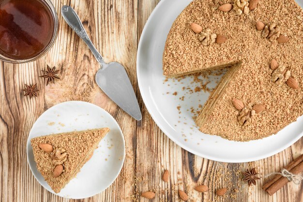 Bolo de mel em camadas doce caseiro com nozes no prato branco na mesa de madeira com uma tigela de mel, canela e badian.