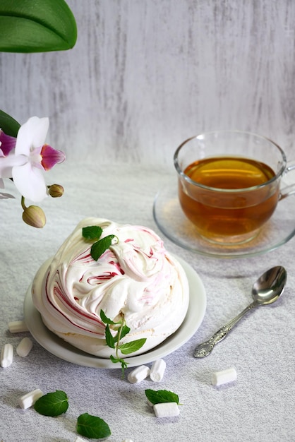 bolo de merengue arejado sobre um fundo claro e uma xícara de chá emoldurada por uma orquídea branca florescendo