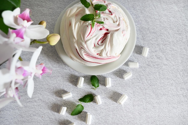 bolo de merengue arejado sobre um fundo claro e uma xícara de chá emoldurada por uma orquídea branca florescendo