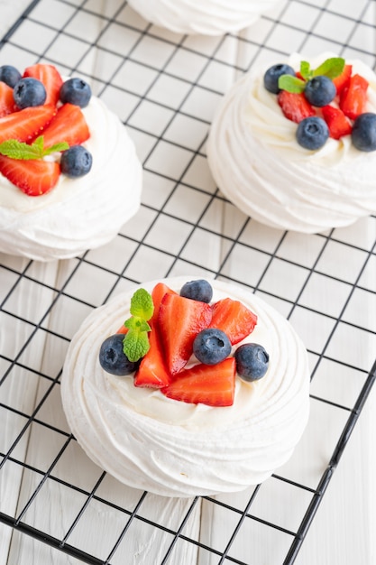 Bolo de merengue Pavlova com chantilly e frutas frescas por cima em uma grade de resfriamento em um fundo branco de madeira. Sobremesa de verão. Copie o espaço.