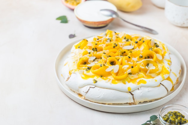 Bolo de merengue Pavlova com manga fresca e maracujá e chantilly sobre fundo de ardósia, pedra ou concreto