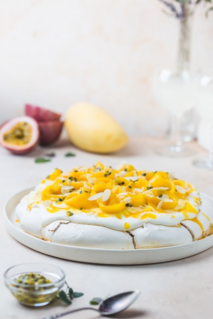 Bolo de merengue pavlova com manga fresca e maracujá e chantilly sobre fundo de ardósia, pedra ou concreto