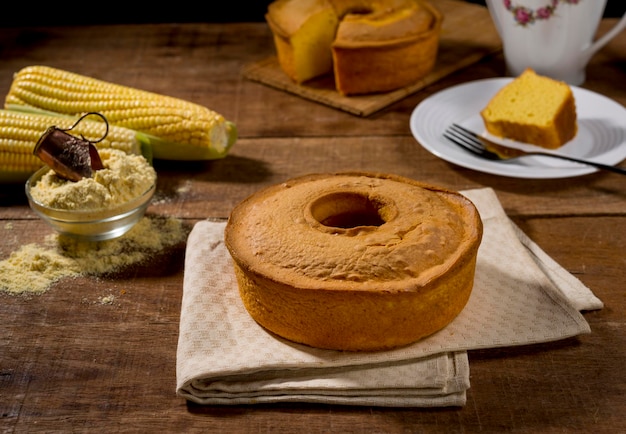 Bolo de milho na mesa de madeira rústica com fatia de milho no prato e bolo no fundo