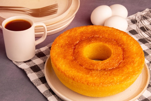 Bolo de milho Pamonha Fuba arredondado caseiro, um café e ovos ao fundo, mesa de piquenique quadriculada