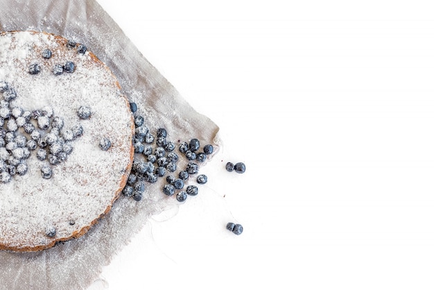 Bolo de mirtilo com bluberries frescas e açúcar em pó em um tecido bege sobre uma superfície branca