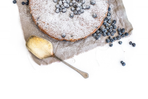 Bolo de mirtilo com bluberries frescas e açúcar em pó em um tecido bege sobre uma superfície branca