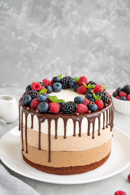 Bolo de mousse de chocolate três com bagas de cobertura de chocolate no topo em um fundo de concreto cinza