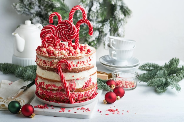 Bolo de muitas camadas de natal decorado com pirulito confete vermelho e  branco em suporte de bolo branco bolas de natal ramos de abeto na mesa de  concreto branco foco seletivo |
