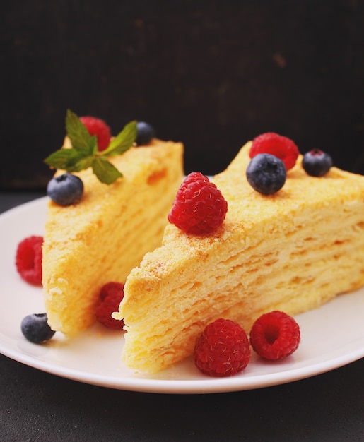 Bolo de Napoleão decorado com framboesas, mirtilos e hortelã em um prato branco sobre um fundo preto