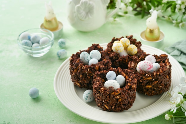 Bolo de ninho de chocolate de Páscoa com mini ovos de chocolate com flores desabrochando de cereja ou maçã na mesa de fundo verde Receita criativa para mesa de Páscoa com decorações de férias Vista superior